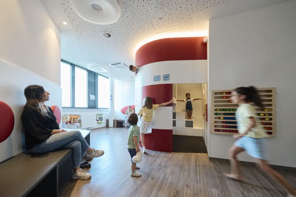 Kinder klettern und spielen in einem Spielbereich mit rot-weißer Wand und einem großen Kugel-Zählrahmen