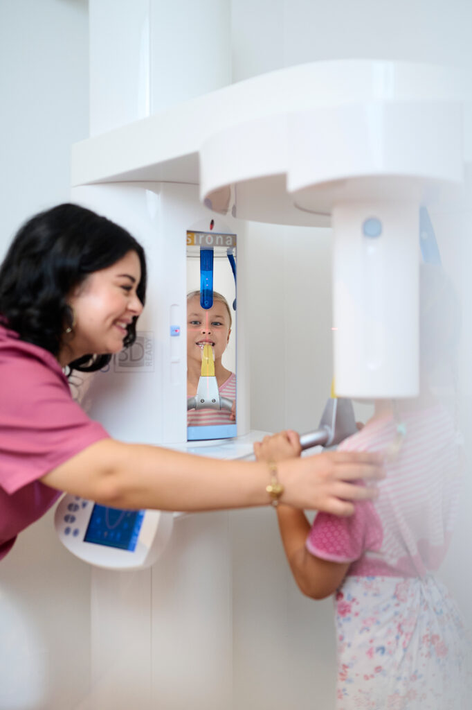 Mitarbeiterin positioniert lächelnd ein Mädchen für eine digitale Röntgenaufnahme im 3D-Röntgengerät